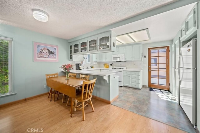 243 N 11th St, Grover Beach, CA 93433 - kitchen featuring white appliances, a peninsula, light countertops, light wood-style floors, and glass insert cabinets