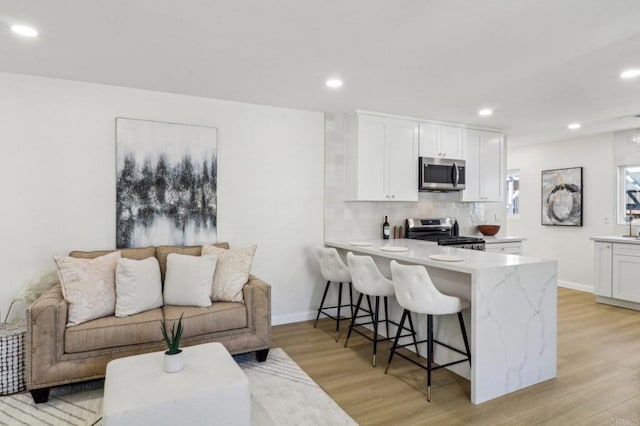 1740 Petra Dr, San Diego, CA 92104 - kitchen with appliances with stainless steel finishes, a breakfast bar, light wood-style floors, white cabinets, and recessed lighting