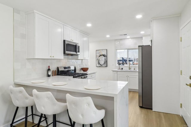 1740 Petra Dr, San Diego, CA 92104 - kitchen featuring stainless steel appliances, decorative backsplash, white cabinets, a kitchen bar, and recessed lighting