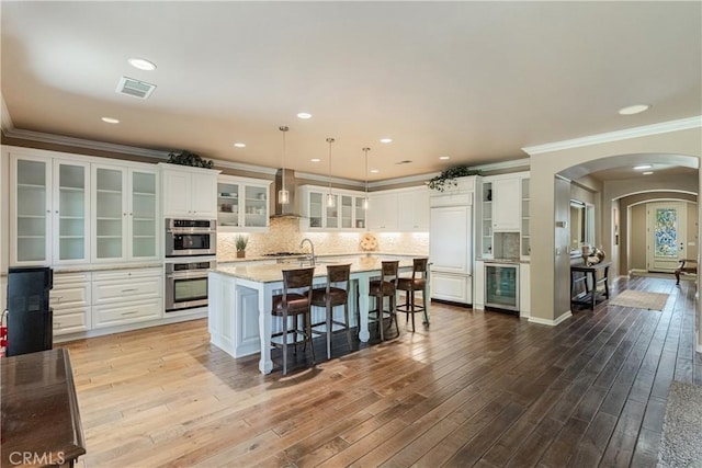36702 Doreen Dr, Murrieta, CA 92563 - kitchen featuring wall chimney exhaust hood, wine cooler, appliances with stainless steel finishes, arched walkways, and ornamental molding