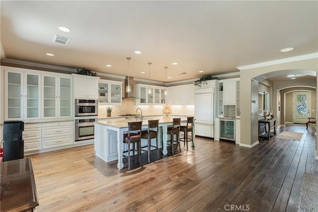 36702 Doreen Dr, Murrieta, CA 92563 - kitchen featuring wall chimney exhaust hood, wine cooler, appliances with stainless steel finishes, ornamental molding, and arched walkways