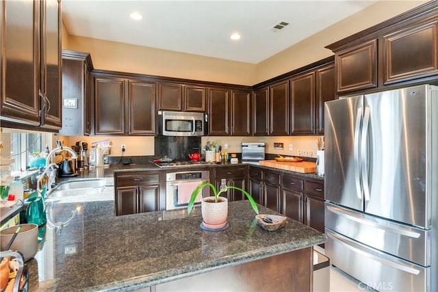 10460 Meadow Lark Ave, Moreno Valley, CA 92557 - kitchen with appliances with stainless steel finishes, dark brown cabinets, a sink, a peninsula, and dark stone counters