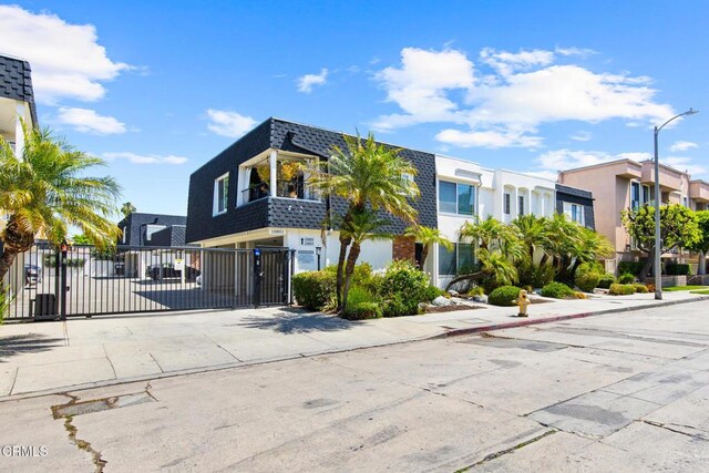 10801 Blix St Unit 2, Toluca Lake, CA 91602 - view of front facade featuring a gate, mansard roof, concrete driveway, stucco siding, and a shingled roof
