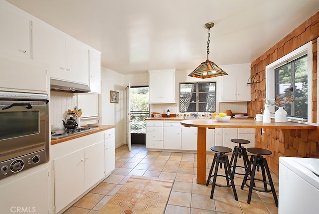 2057 Oakwood St, Pasadena, CA 91104 - kitchen with under cabinet range hood, electric cooktop, decorative backsplash, white cabinets, and decorative light fixtures