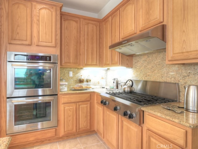 15585 Marnie Pl, Fontana, CA 92336 - kitchen with under cabinet range hood, appliances with stainless steel finishes, backsplash, light stone countertops, and light tile patterned flooring