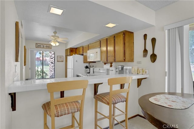 69723 Encanto Ct, Rancho Mirage, CA 92270 - kitchen with white appliances, brown cabinetry, ceiling fan, a peninsula, and tile countertops
