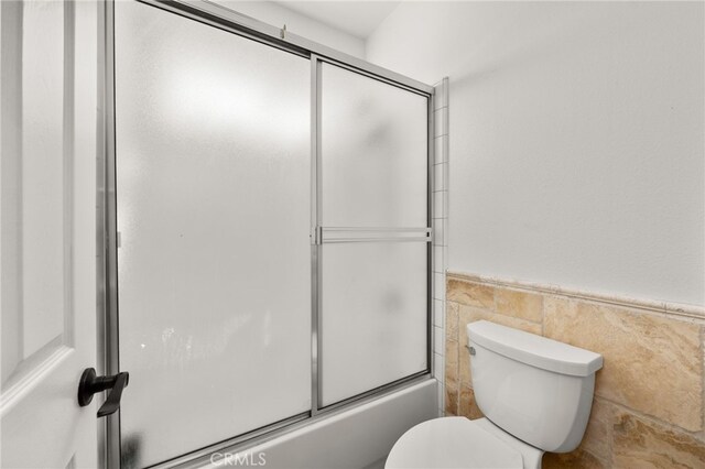 18936 Summerleaf Ln, Riverside, CA 92504 - bathroom featuring a wainscoted wall, toilet, combined bath / shower with glass door, and tile walls