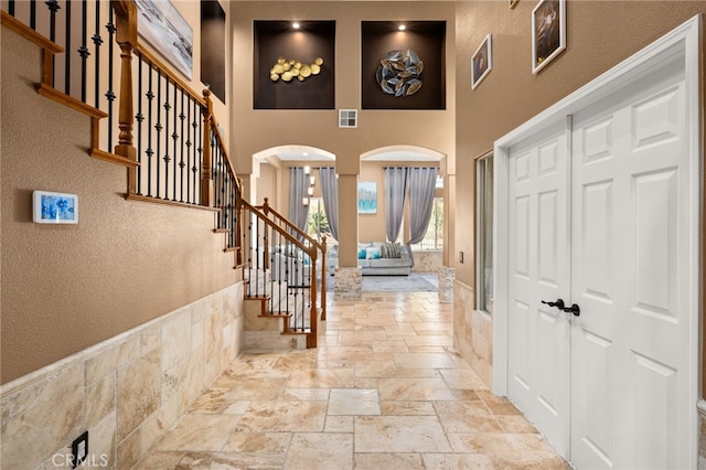 18936 Summerleaf Ln, Riverside, CA 92504 - foyer entrance featuring stone tile floors, a towering ceiling, arched walkways, stairs, and a textured wall