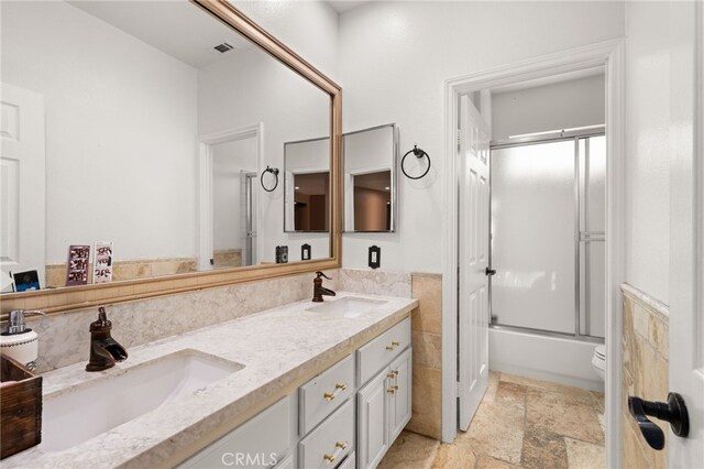 18936 Summerleaf Ln, Riverside, CA 92504 - full bathroom featuring double vanity, toilet, stone tile flooring, enclosed tub / shower combo, and tile walls