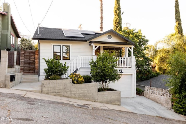4865 Granada St, Los Angeles, CA 90042 - view of front of property with concrete driveway, roof mounted solar panels, an attached garage, a shingled roof, and covered porch