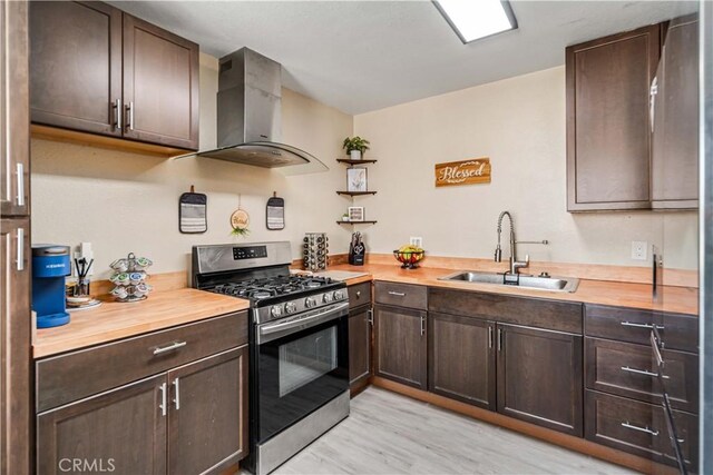 24438 Sage Ave, Boron, CA 93516 - kitchen featuring gas range, wall chimney range hood, a sink, dark brown cabinetry, and light wood-style floors