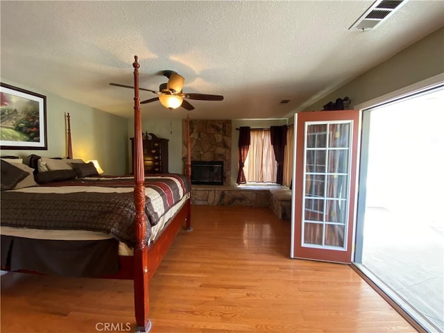 7614 Calpella Ave, Hesperia, CA 92345 - bedroom with light wood-style floors, a textured ceiling, multiple windows, ceiling fan, and a stone fireplace