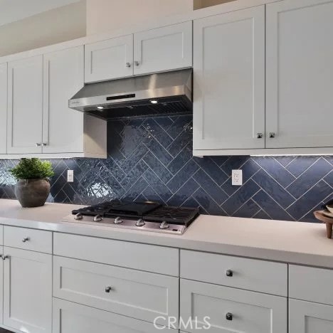 27225 Cranmore Way Unit 302, Valencia, CA 91381 - kitchen with under cabinet range hood, stainless steel gas stovetop, white cabinetry, tasteful backsplash, and light countertops