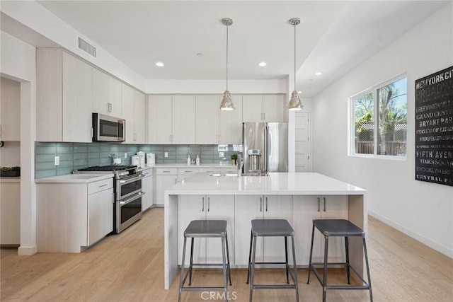 1746 Garfield Pl Unit 203, Los Angeles, CA 90028 - kitchen featuring appliances with stainless steel finishes, light countertops, a breakfast bar, light wood-type flooring, and tasteful backsplash