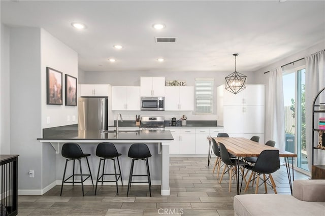 3611 Highclere Way, Clovis, CA 93619 - kitchen featuring stainless steel appliances, dark countertops, a peninsula, a kitchen breakfast bar, and wood finish floors