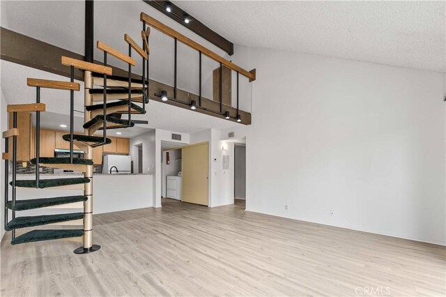 105 Tangelo Unit 400, Irvine, CA 92618 - unfurnished living room featuring high vaulted ceiling, stairway, light wood-style floors, washer and dryer, and a textured ceiling