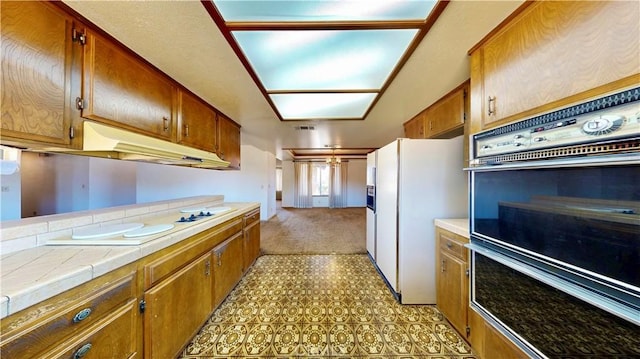 20061 Seneca Rd, Apple Valley, CA 92307 - kitchen featuring white refrigerator with ice dispenser, under cabinet range hood, tile countertops, brown cabinets, and light colored carpet