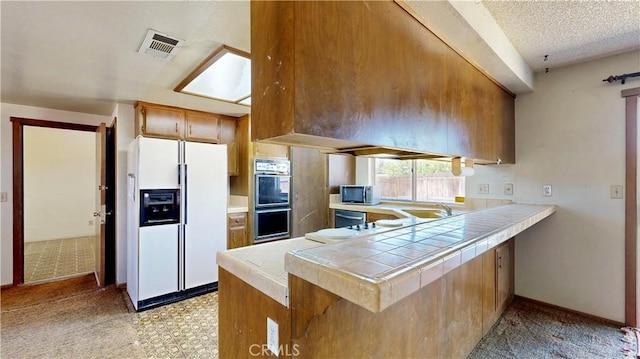 20061 Seneca Rd, Apple Valley, CA 92307 - kitchen with white fridge with ice dispenser, double oven, stainless steel microwave, a peninsula, and tile countertops