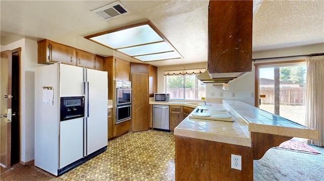 20061 Seneca Rd, Apple Valley, CA 92307 - kitchen with appliances with stainless steel finishes, tile countertops, a sink, brown cabinets, and a peninsula