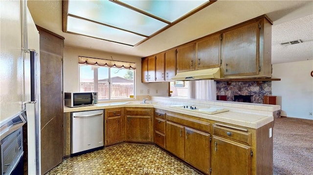 20061 Seneca Rd, Apple Valley, CA 92307 - kitchen featuring stainless steel appliances, a peninsula, brown cabinets, a textured ceiling, and a fireplace