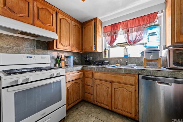 146 Padre Tullio Dr, San Ysidro, CA 92173 - kitchen with white gas stove, stainless steel dishwasher, under cabinet range hood, brown cabinets, and tasteful backsplash