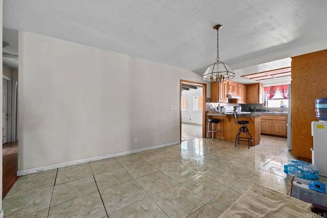 146 Padre Tullio Dr, San Ysidro, CA 92173 - kitchen featuring a kitchen breakfast bar, under cabinet range hood, baseboards, a peninsula, and a chandelier