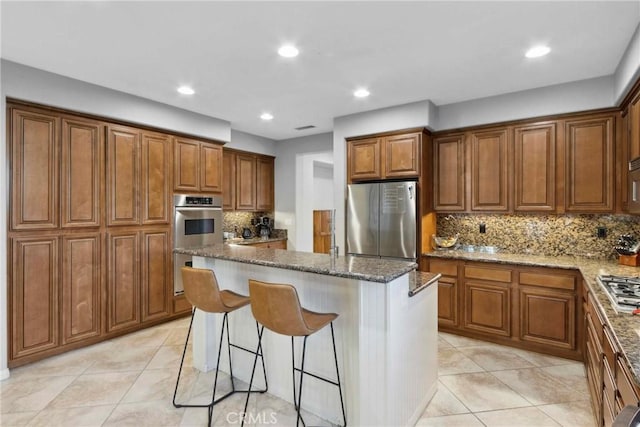 45614 Hawk Ct, Temecula, CA 92592 - kitchen with appliances with stainless steel finishes, brown cabinets, a center island, dark stone counters, and a kitchen breakfast bar