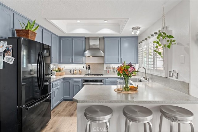 19431 Ranch Ln Unit 101, Huntington Beach, CA 92648 - kitchen featuring stainless steel appliances, wall chimney range hood, a sink, a peninsula, and a raised ceiling
