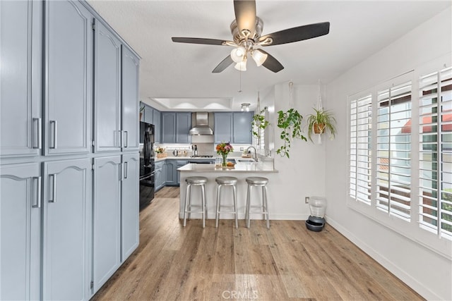 19431 Ranch Ln Unit 101, Huntington Beach, CA 92648 - kitchen with freestanding refrigerator, a peninsula, wall chimney range hood, light wood-type flooring, and a kitchen breakfast bar