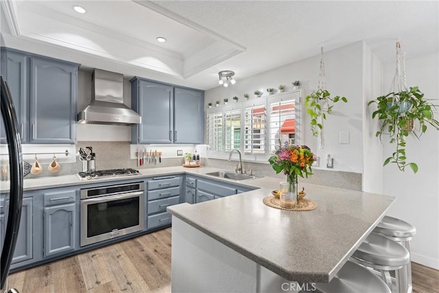 19431 Ranch Ln Unit 101, Huntington Beach, CA 92648 - kitchen with stainless steel appliances, wall chimney exhaust hood, a tray ceiling, a sink, and a peninsula