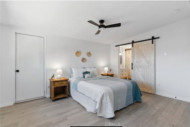 7686 Deer Trl, Yucca Valley, CA 92284 - bedroom featuring a barn door, light wood-type flooring, ceiling fan, and ensuite bathroom