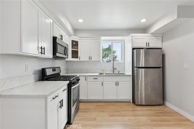 2806 Cudahy St, Huntington Park, CA 90255 - kitchen featuring appliances with stainless steel finishes, light countertops, white cabinetry, a sink, and light wood-type flooring