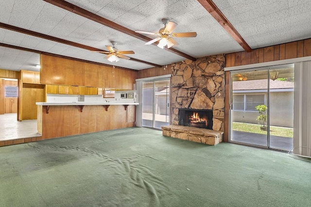 13321 Prospect Ave, North Tustin, CA 92705 - unfurnished living room with wood walls, beam ceiling, carpet floors, a stone fireplace, and a ceiling fan