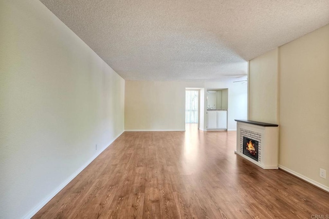 2564 Navarra Dr Unit 115, Carlsbad, CA 92009 - unfurnished living room featuring a textured ceiling, a warm lit fireplace, wood finished floors, and baseboards
