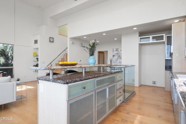 1196 Montecito Dr, Los Angeles, CA 90031 - kitchen with light wood-type flooring, dark stone countertops, recessed lighting, a towering ceiling, and a kitchen island with sink