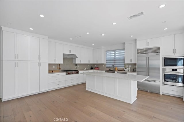 113 Imagination Trl, Irvine, CA 92620 - kitchen with stainless steel appliances, under cabinet range hood, a center island, white cabinetry, and light wood finished floors