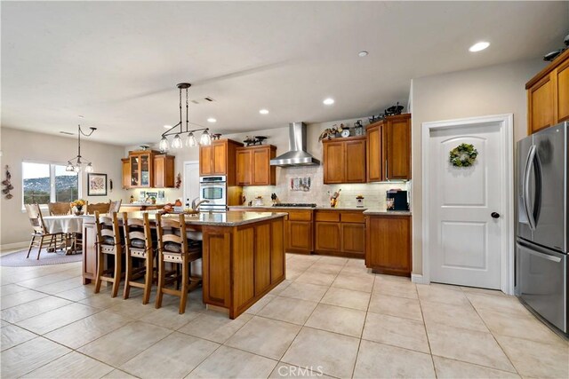 10204 Mount Olympus Valley Rd, Fallbrook, CA 92028 - kitchen with freestanding refrigerator, wall chimney range hood, brown cabinetry, light tile patterned flooring, and recessed lighting