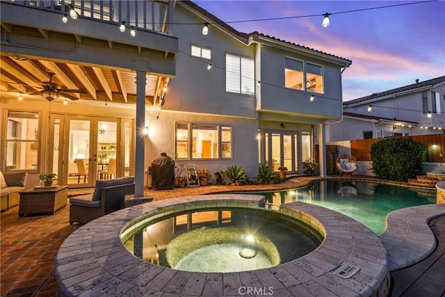 112 Del Cabo, San Clemente, CA 92673 - back of house at dusk featuring french doors, a balcony, a pool with connected hot tub, a ceiling fan, and stucco siding