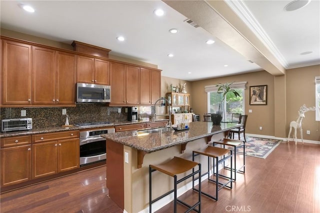 7151 Stockton Dr, Eastvale, CA 92880 - kitchen with stainless steel appliances, a sink, brown cabinetry, decorative backsplash, and a breakfast bar area