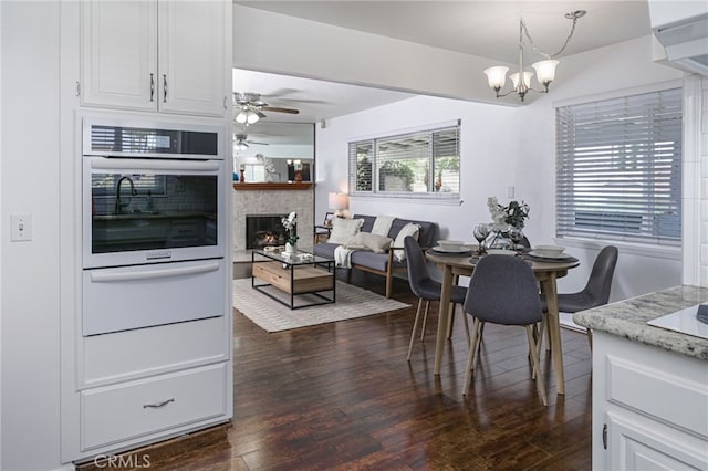 2620 W Cobblestone Rd, La Habra, CA 90631 - dining space with dark wood-type flooring, a chandelier, a ceiling fan, and a warm lit fireplace