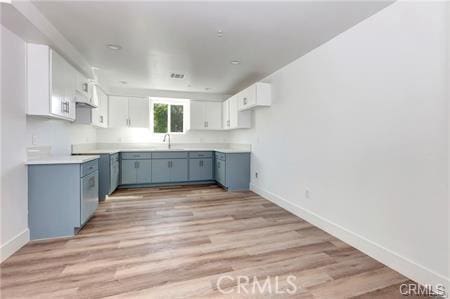 8418 S Main St, Los Angeles, CA 90003 - kitchen with blue cabinets, baseboards, light wood-style floors, white cabinets, and a sink