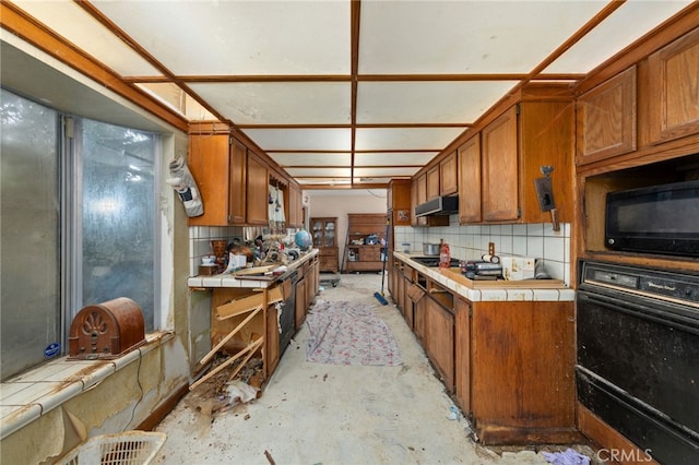 13397 Robin Ct, Yucaipa, CA 92399 - kitchen with tile countertops, black appliances, under cabinet range hood, and brown cabinetry