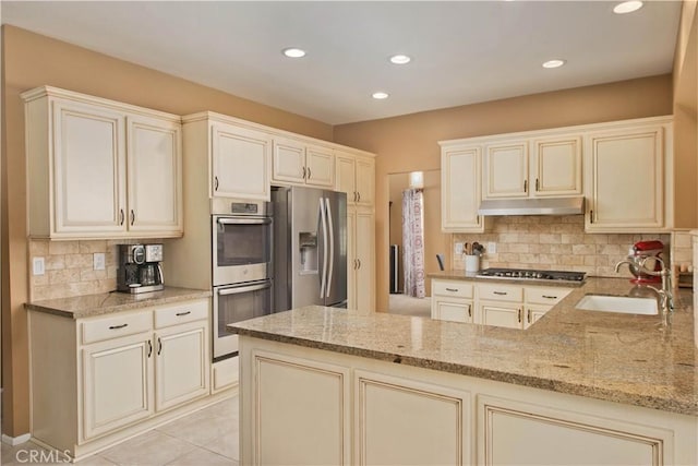 22447 Poplar St, Saugus, CA 91390 - kitchen featuring appliances with stainless steel finishes, under cabinet range hood, a sink, light stone countertops, and a peninsula