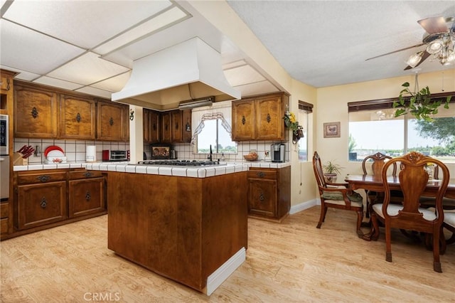3298 N Zediker Ave, Sanger, CA 93657 - kitchen with custom range hood, light wood-style flooring, ceiling fan, tile counters, and decorative backsplash