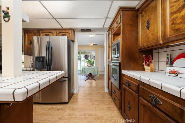 3298 N Zediker Ave, Sanger, CA 93657 - kitchen featuring stainless steel appliances, tile countertops, light wood-style floors, decorative backsplash, and a drop ceiling