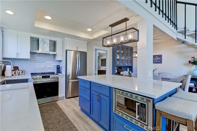 259 Calle Aragon Unit A, Laguna Woods, CA 92637 - kitchen featuring appliances with stainless steel finishes, wall chimney range hood, blue cabinetry, a sink, and white cabinetry