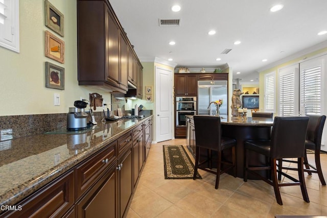 4003 Galapagos Way, Oxnard, CA 93035 - kitchen with appliances with stainless steel finishes, a breakfast bar area, ornamental molding, light tile patterned floors, and dark stone countertops