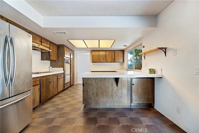 6164 Amberwood Dr, Rancho Cucamonga, CA 91701 - kitchen featuring freestanding refrigerator, a peninsula, brown cabinets, cooktop, and a sink