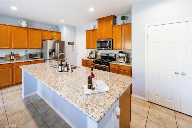 31786 Sorrel Run Ct, Menifee, CA 92584 - kitchen with appliances with stainless steel finishes, a sink, light tile patterned flooring, brown cabinetry, and a center island with sink