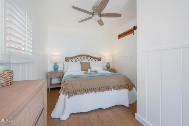 244 Cahuenga Dr, Oxnard, CA 93035 - bedroom with a barn door, hardwood / wood-style floors, a decorative wall, wainscoting, and a ceiling fan